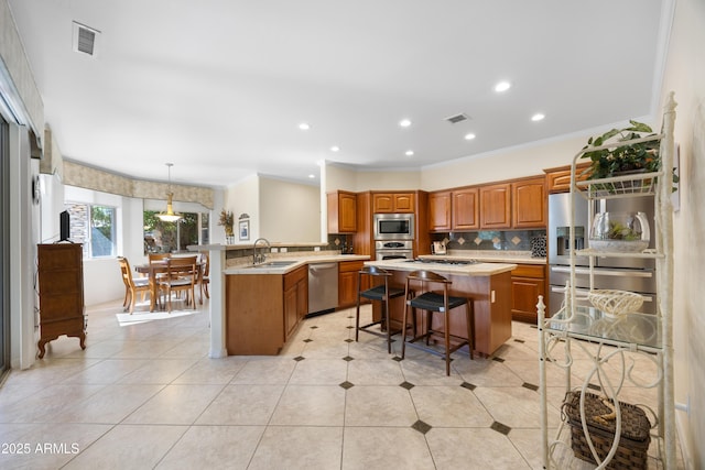 kitchen featuring a kitchen bar, sink, hanging light fixtures, a center island with sink, and stainless steel appliances