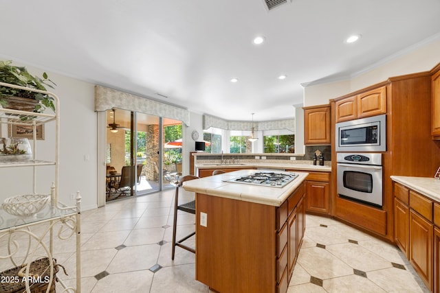 kitchen with a kitchen island, appliances with stainless steel finishes, backsplash, ornamental molding, and light tile patterned floors