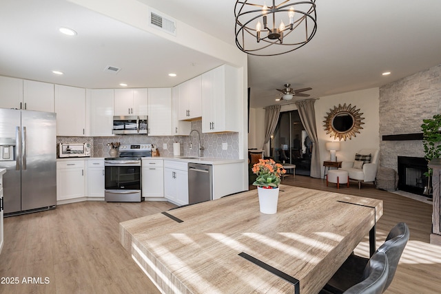 kitchen featuring white cabinetry, sink, backsplash, hanging light fixtures, and stainless steel appliances