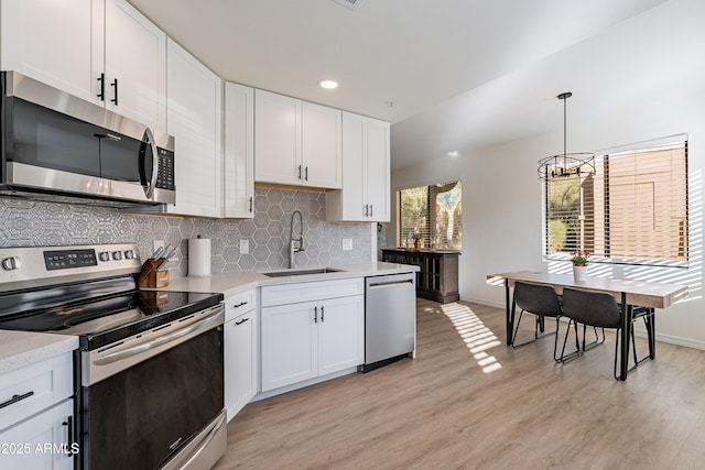 kitchen with sink, appliances with stainless steel finishes, tasteful backsplash, white cabinets, and decorative light fixtures