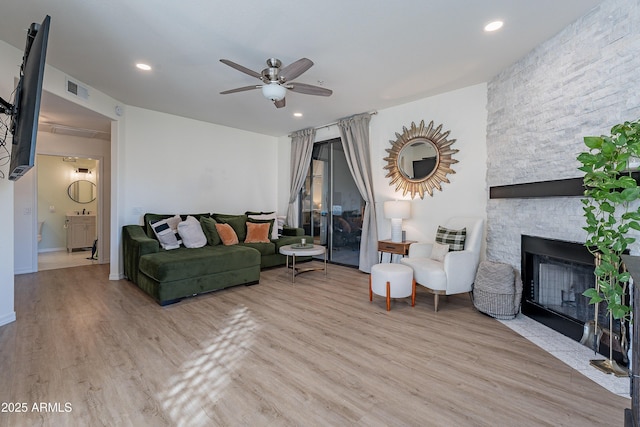 living room featuring ceiling fan, a stone fireplace, and light wood-type flooring