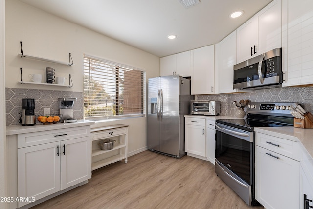 kitchen with tasteful backsplash, white cabinetry, appliances with stainless steel finishes, and light wood-type flooring