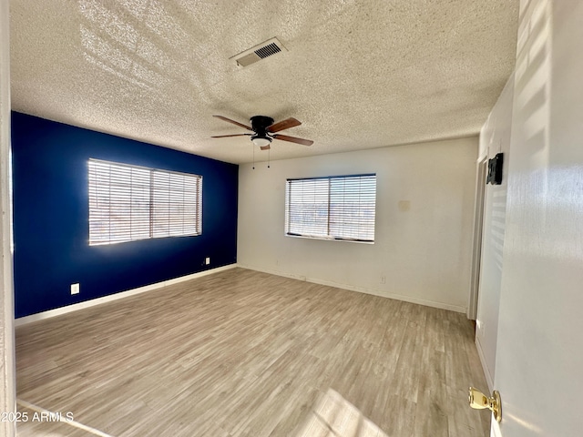 empty room featuring a textured ceiling, a ceiling fan, baseboards, visible vents, and light wood-style floors