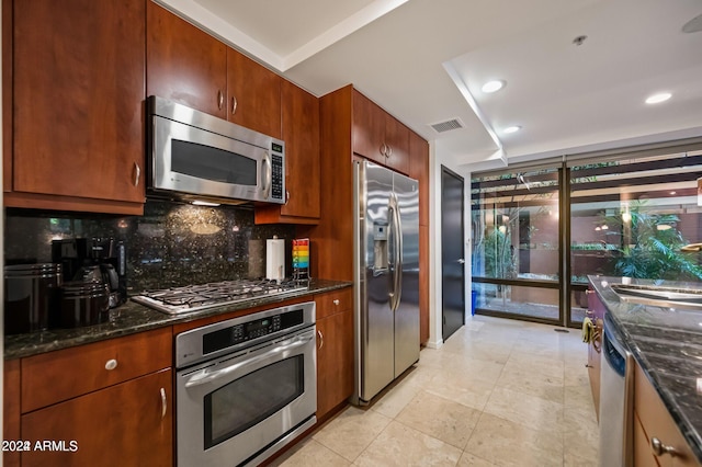 kitchen with appliances with stainless steel finishes, backsplash, dark stone counters, sink, and light tile patterned floors