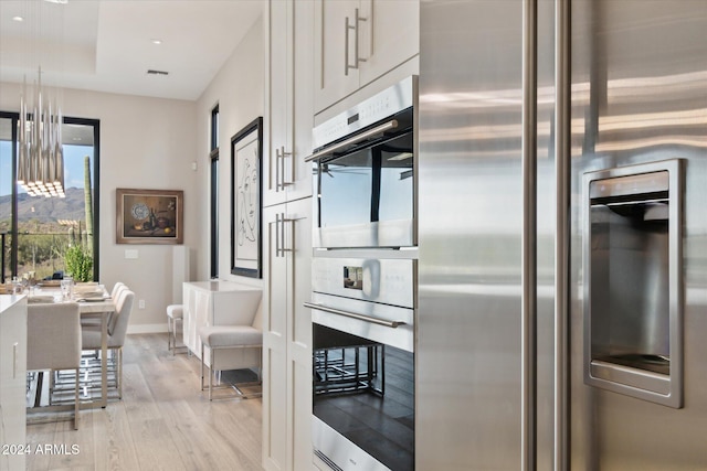 kitchen with appliances with stainless steel finishes, white cabinetry, and light wood-type flooring