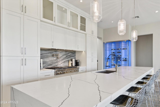 kitchen featuring white cabinets, light stone countertops, sink, a kitchen breakfast bar, and stainless steel gas stovetop