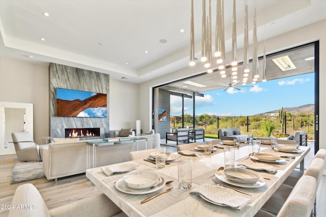 dining room featuring a raised ceiling, a premium fireplace, an inviting chandelier, light wood-type flooring, and a mountain view