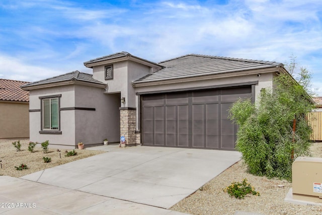 prairie-style house with stucco siding, driveway, a tile roof, stone siding, and an attached garage