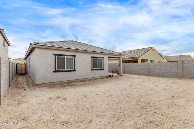 rear view of house with stucco siding, a fenced backyard, and a tiled roof