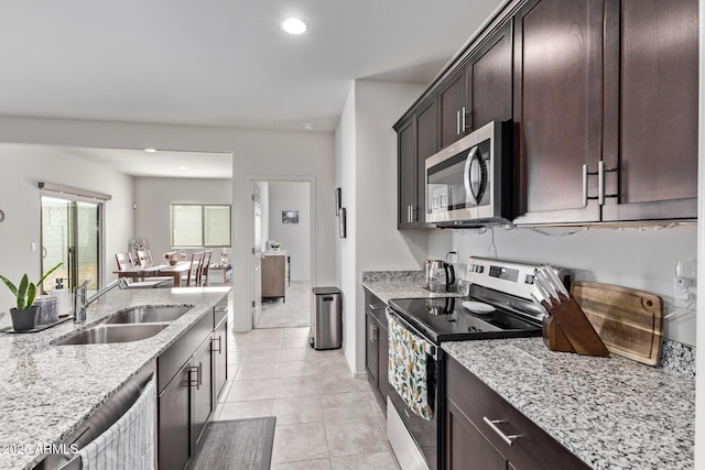 kitchen with a sink, light stone countertops, appliances with stainless steel finishes, and light tile patterned flooring