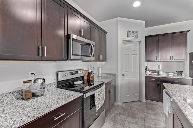 kitchen featuring dark brown cabinetry, light tile patterned floors, stainless steel appliances, and light stone counters