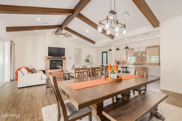 dining room with a fireplace, lofted ceiling with beams, a healthy amount of sunlight, and light wood-type flooring