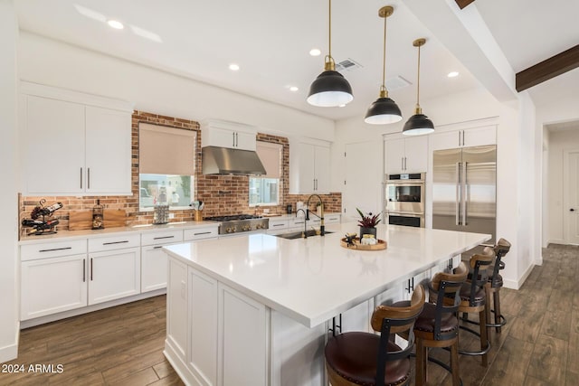 kitchen featuring decorative light fixtures, white cabinets, decorative backsplash, a large island with sink, and stainless steel appliances