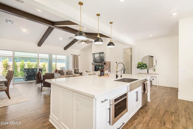 kitchen with sink, white cabinetry, lofted ceiling with beams, a brick fireplace, and hanging light fixtures