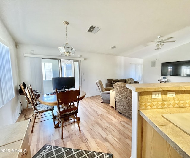 dining space with light wood-style flooring, ceiling fan, a chandelier, and lofted ceiling
