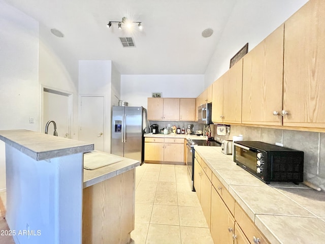 kitchen with stainless steel appliances, light brown cabinets, tile counters, light tile patterned floors, and lofted ceiling