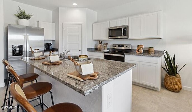 kitchen featuring appliances with stainless steel finishes, white cabinetry, dark stone counters, sink, and a center island with sink