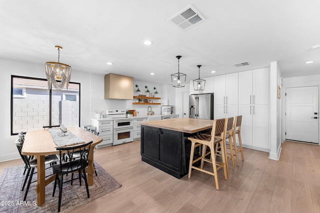 kitchen with high end refrigerator, light hardwood / wood-style flooring, double oven range, a kitchen island, and white cabinets