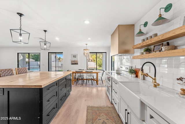 kitchen featuring pendant lighting, wood counters, white cabinets, a center island, and white appliances