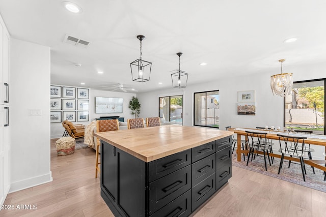 kitchen with butcher block countertops, a kitchen island, pendant lighting, and light hardwood / wood-style floors