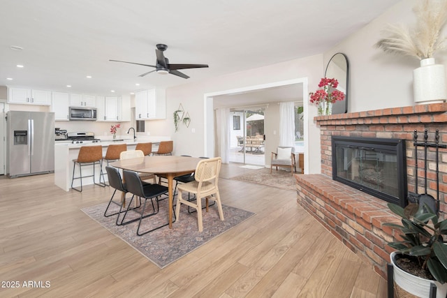 dining room featuring ceiling fan, light wood-type flooring, and a fireplace