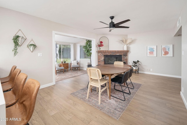 dining area with a brick fireplace, ceiling fan, and light hardwood / wood-style flooring