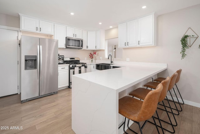 kitchen featuring a breakfast bar, stainless steel appliances, sink, light hardwood / wood-style floors, and white cabinetry