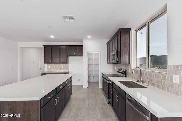 kitchen with appliances with stainless steel finishes, a kitchen island, decorative backsplash, sink, and dark brown cabinets