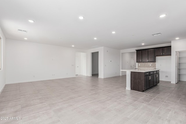 kitchen featuring dark brown cabinets, a kitchen island with sink, and tasteful backsplash