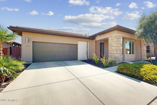 view of front of home featuring driveway, stone siding, stucco siding, fence, and an attached garage