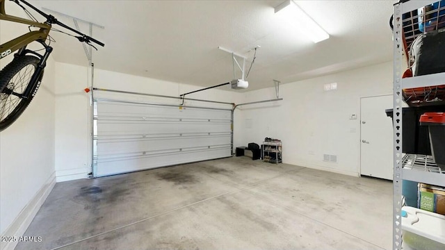 garage featuring a garage door opener, visible vents, and baseboards