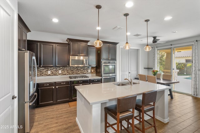 kitchen with pendant lighting, light hardwood / wood-style flooring, stainless steel appliances, a kitchen breakfast bar, and a center island with sink