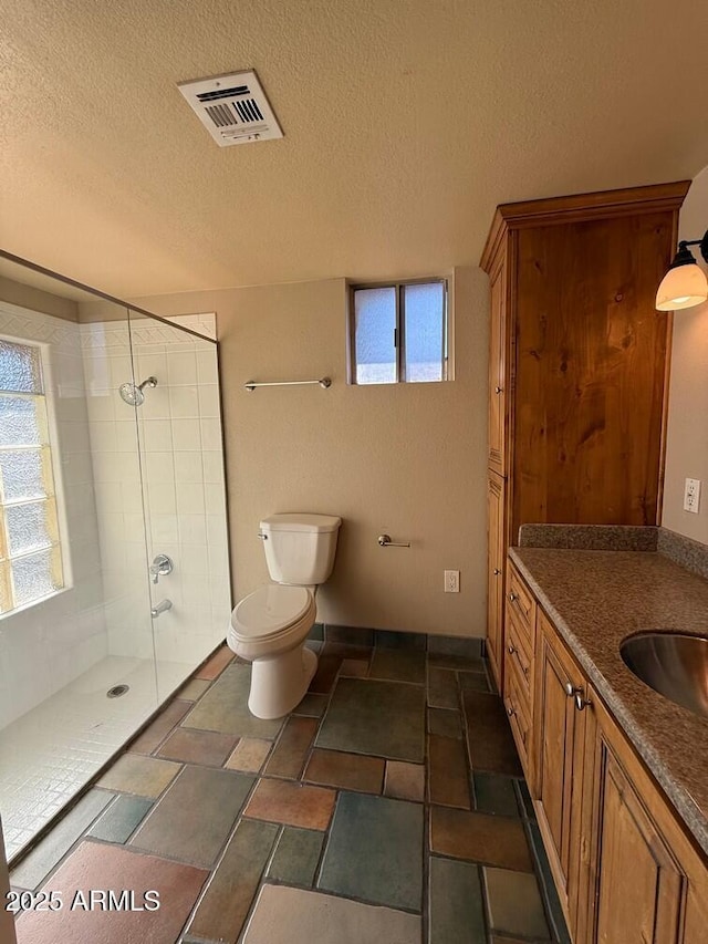 bathroom with vanity, tiled shower, a textured ceiling, and toilet