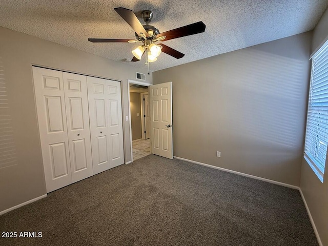 unfurnished bedroom featuring ceiling fan, a closet, a textured ceiling, and dark colored carpet