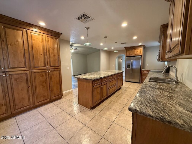 kitchen featuring sink, stainless steel fridge, a kitchen island, pendant lighting, and dark stone counters