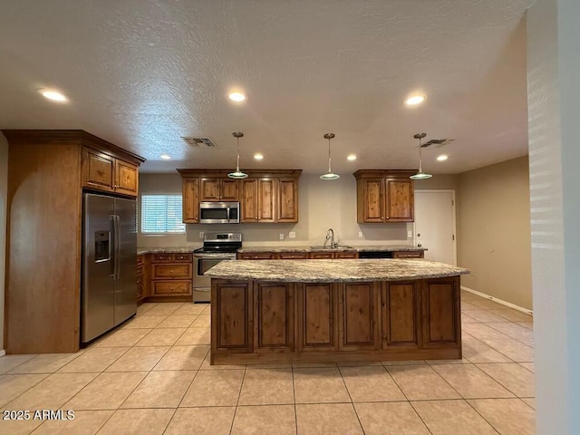 kitchen featuring decorative light fixtures, stainless steel appliances, and a center island with sink