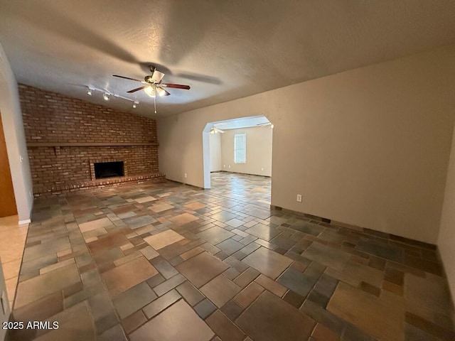 unfurnished living room featuring ceiling fan, vaulted ceiling, a brick fireplace, and a textured ceiling