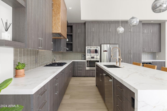 kitchen with decorative backsplash, hanging light fixtures, light hardwood / wood-style flooring, wall chimney exhaust hood, and stainless steel appliances