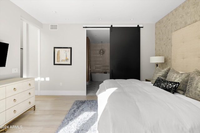 bedroom with a barn door, light hardwood / wood-style floors, and ensuite bath