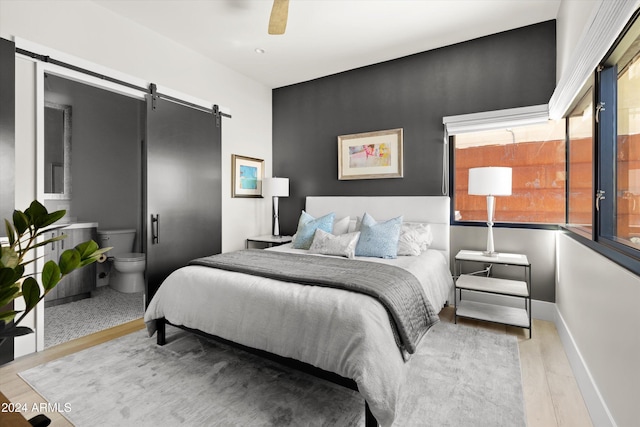 bedroom featuring a barn door, light wood-type flooring, and ceiling fan