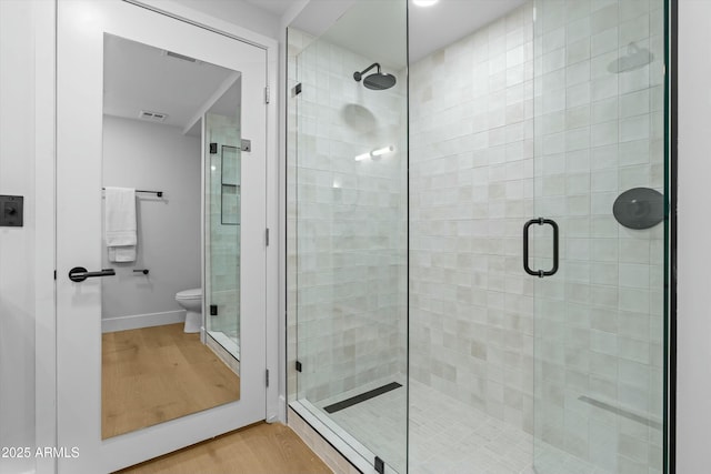 bathroom with a stall shower, baseboards, visible vents, toilet, and wood finished floors