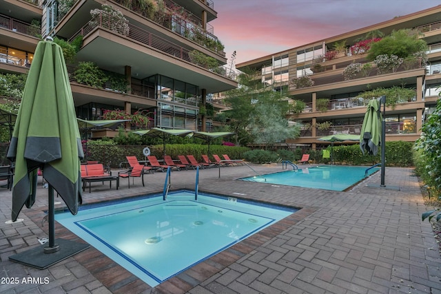 pool at dusk with a patio, a community pool, and a hot tub