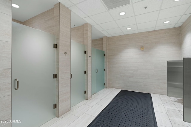 full bathroom featuring tile patterned flooring, a paneled ceiling, visible vents, tile walls, and a stall shower