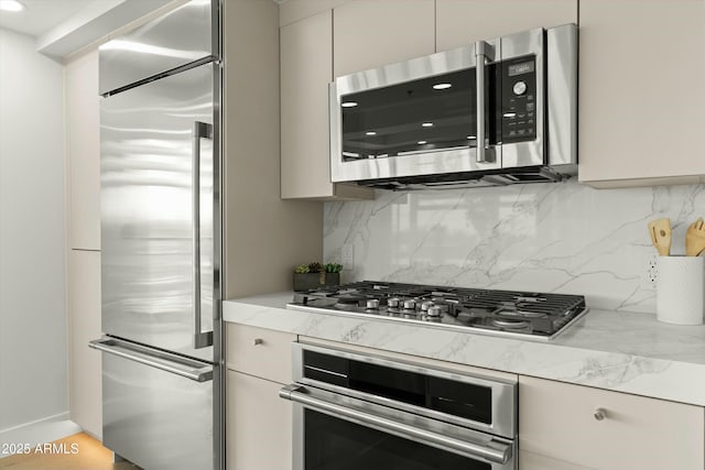 kitchen featuring stainless steel appliances, backsplash, light stone counters, and modern cabinets