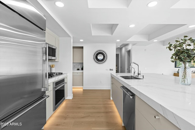 kitchen featuring a tray ceiling, light wood finished floors, recessed lighting, appliances with stainless steel finishes, and a sink