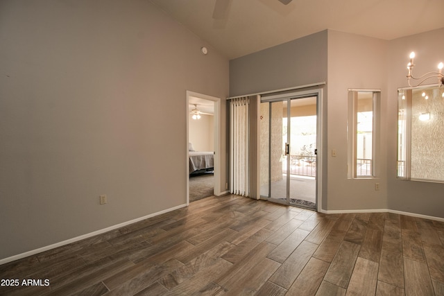 spare room with dark wood-type flooring, high vaulted ceiling, and ceiling fan with notable chandelier