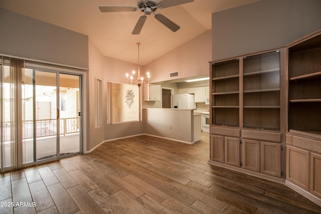 unfurnished dining area with ceiling fan with notable chandelier, dark wood-type flooring, and high vaulted ceiling