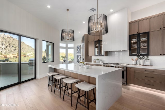 kitchen featuring high end stainless steel range oven, decorative light fixtures, light hardwood / wood-style flooring, a chandelier, and an island with sink