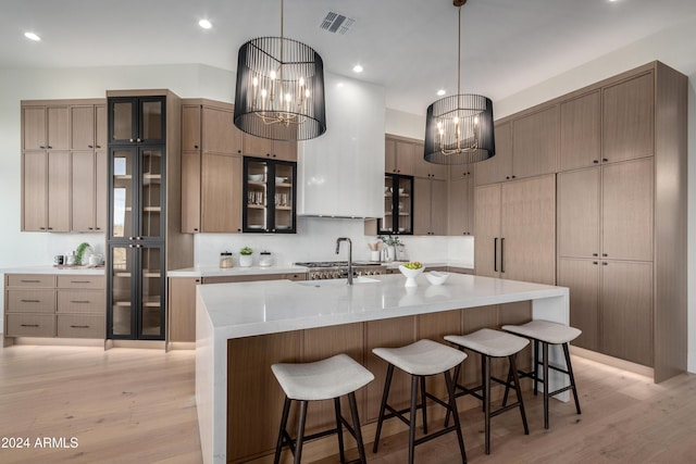 kitchen with a spacious island, sink, hanging light fixtures, light hardwood / wood-style flooring, and a notable chandelier