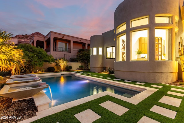 pool at dusk featuring pool water feature